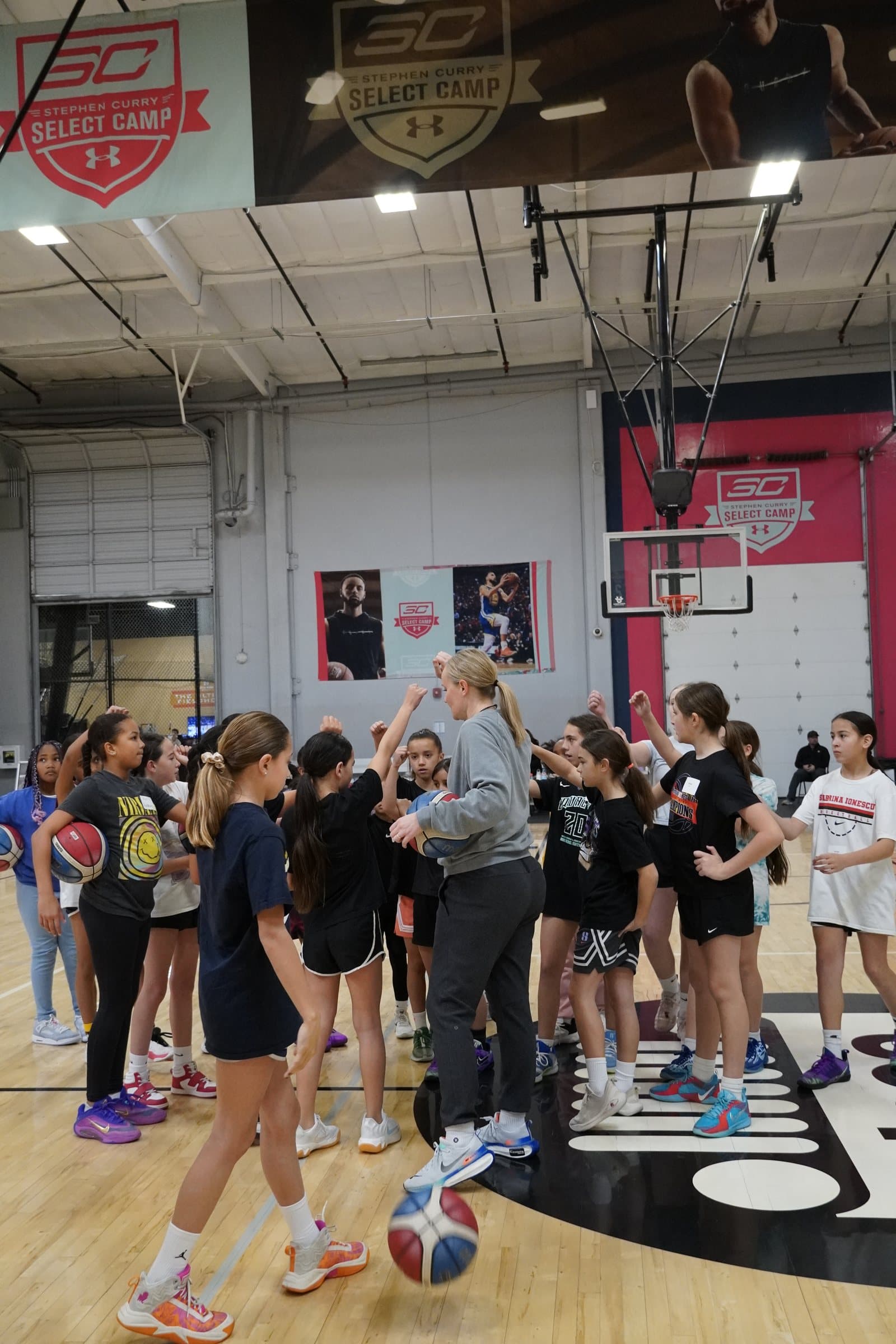 Players and coaches huddle in the middle of the court at an ISI all-girls basketball clinic.